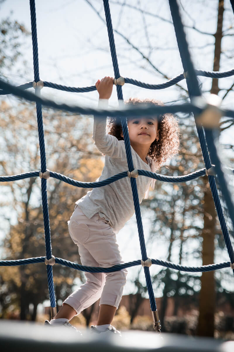 Portrait d'une petite fille escaladant une structure sur une aire de jeux pour enfants